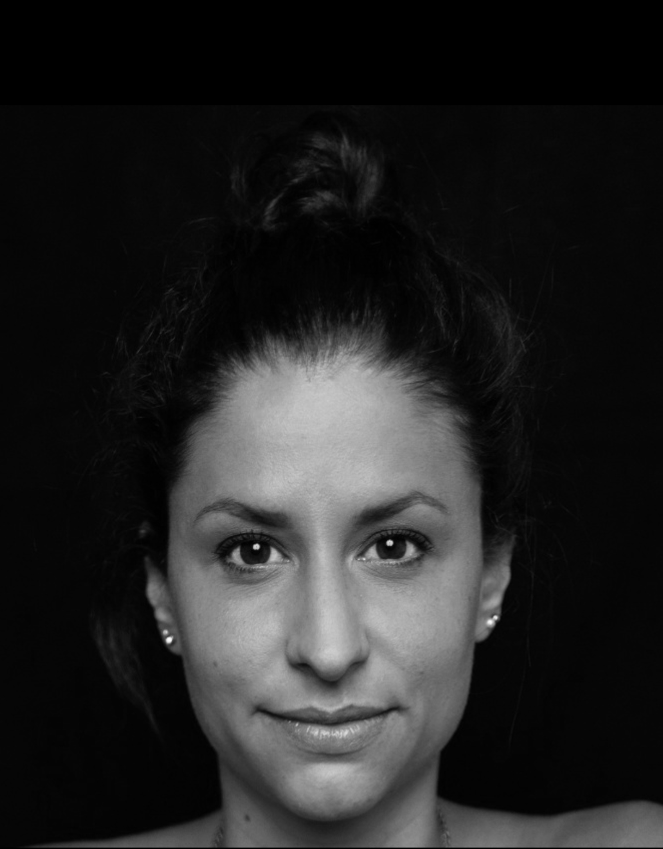 Coachin Alina Jessl Bild Porträt einer Frau mit dunklem Haar als Dutt, lächelnd und vor schwarzem Hintergrund. Die Abbildung zeigt nur den Kopf, ist schwarz weiß